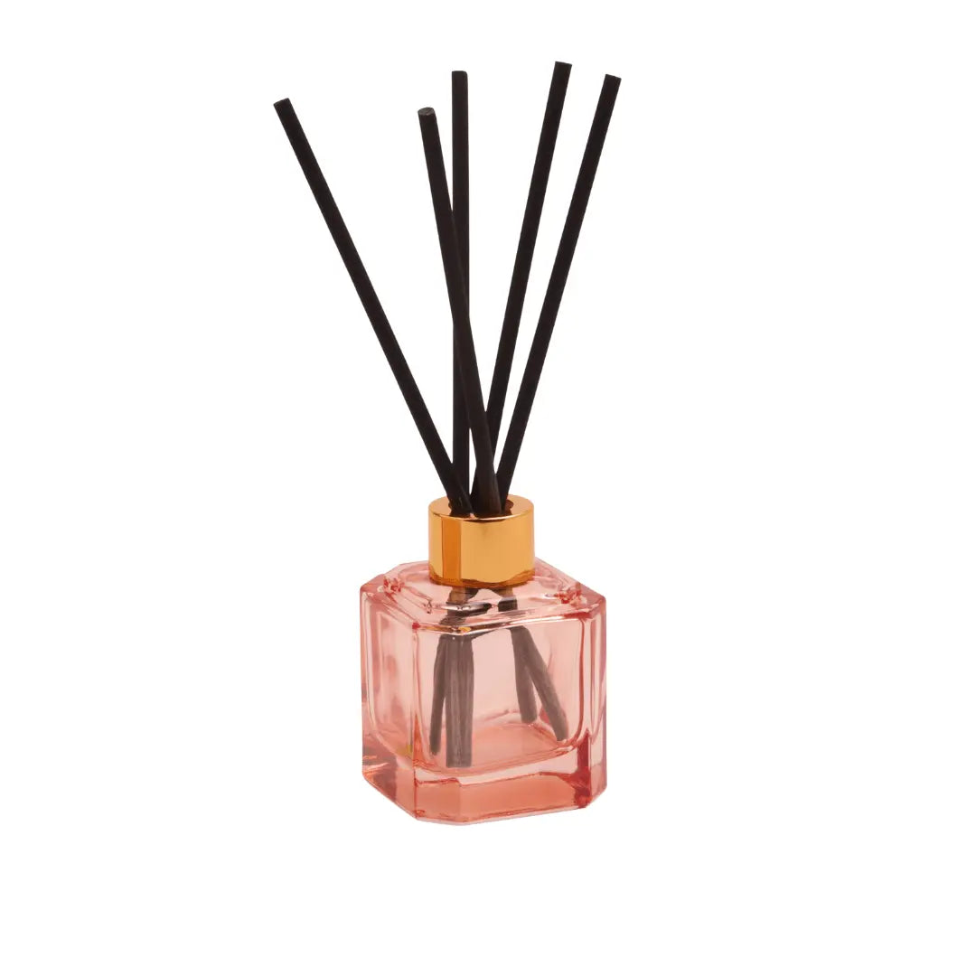 The Saffron Rose - Botanica Diffuser 2.88 oz features a pink glass design with a gold cap and black reeds, filling your space with an elegant saffron rose scent—a modern home fragrance statement against a white background.