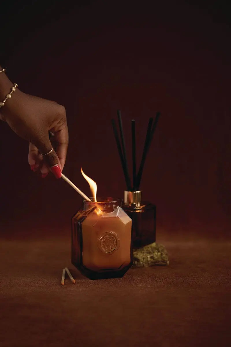A hand uses the Leather + Smoke - Botanica Diffuser 2.88 oz, filling the space with its rich aroma.