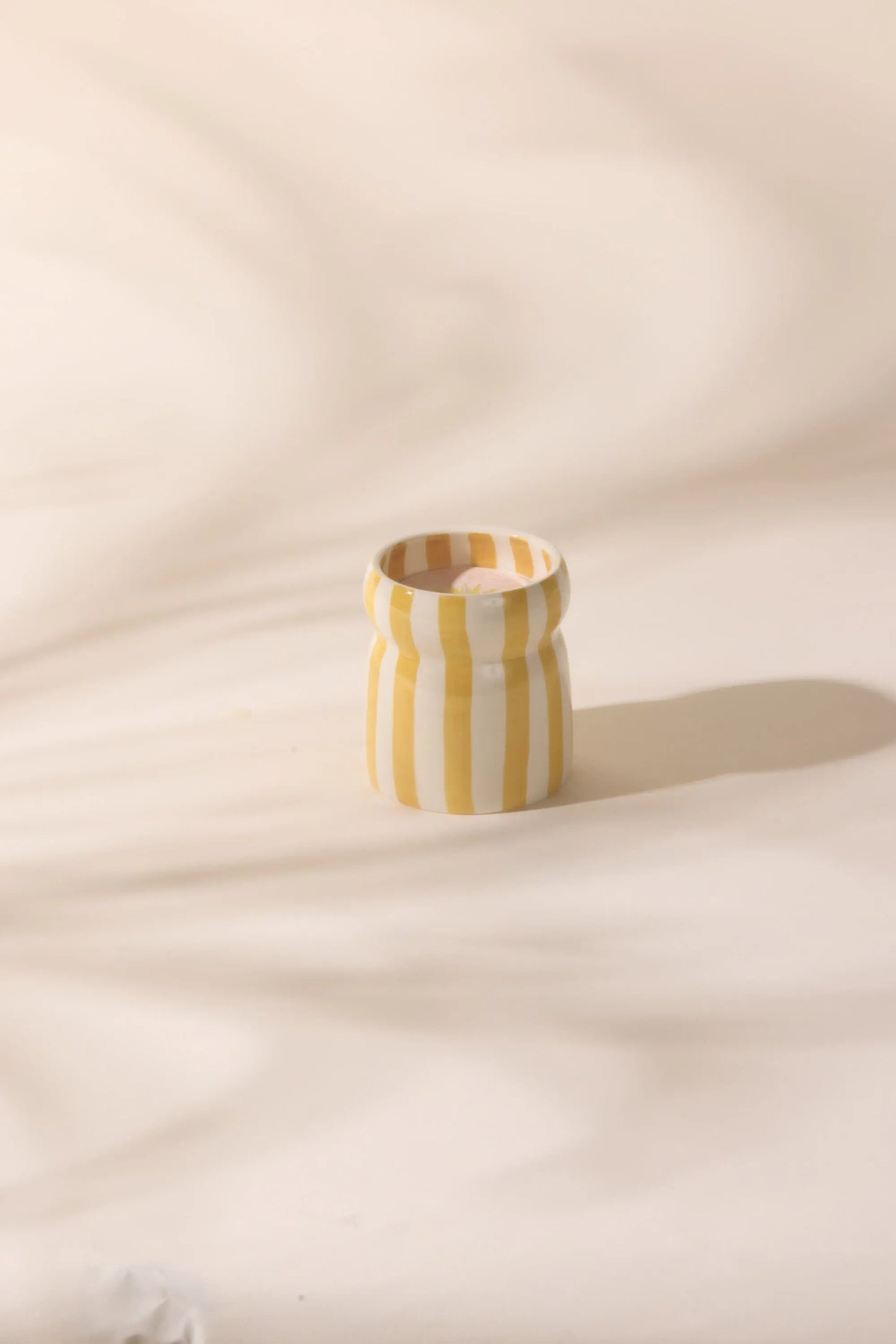 The Gold Coast - Cabana 6.5 oz Candle features a small ceramic vessel with vertical yellow and white stripes, perfect for filling your home with calming coastal scents.
