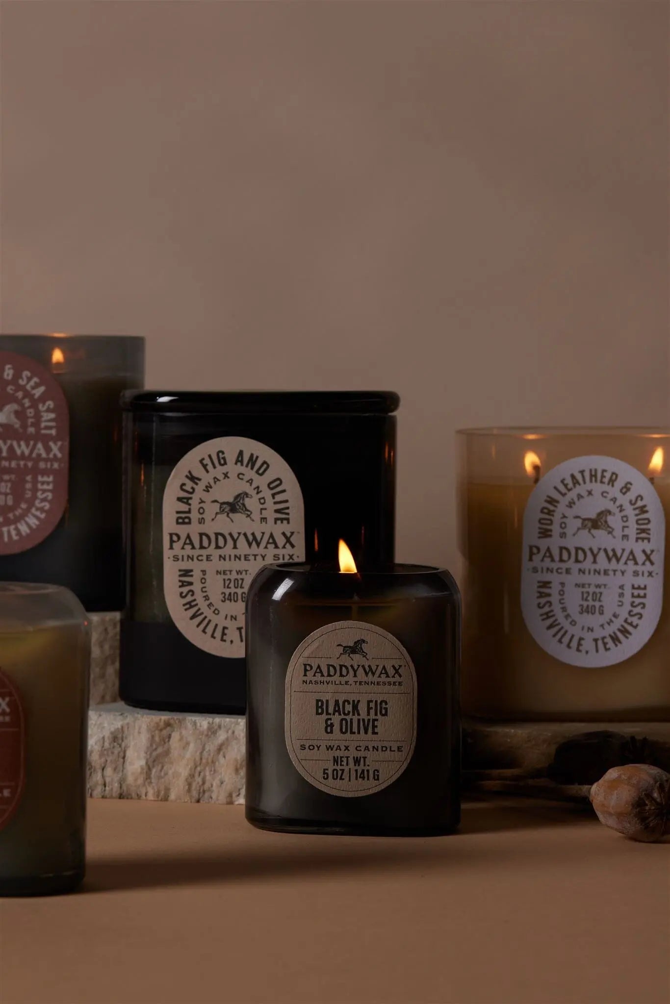 The Black Fig & Olive - Vista 5 oz Candle adds a luxurious scent and modern style to any space, arranged on a stone surface against a beige backdrop—perfect for contemporary home decor.