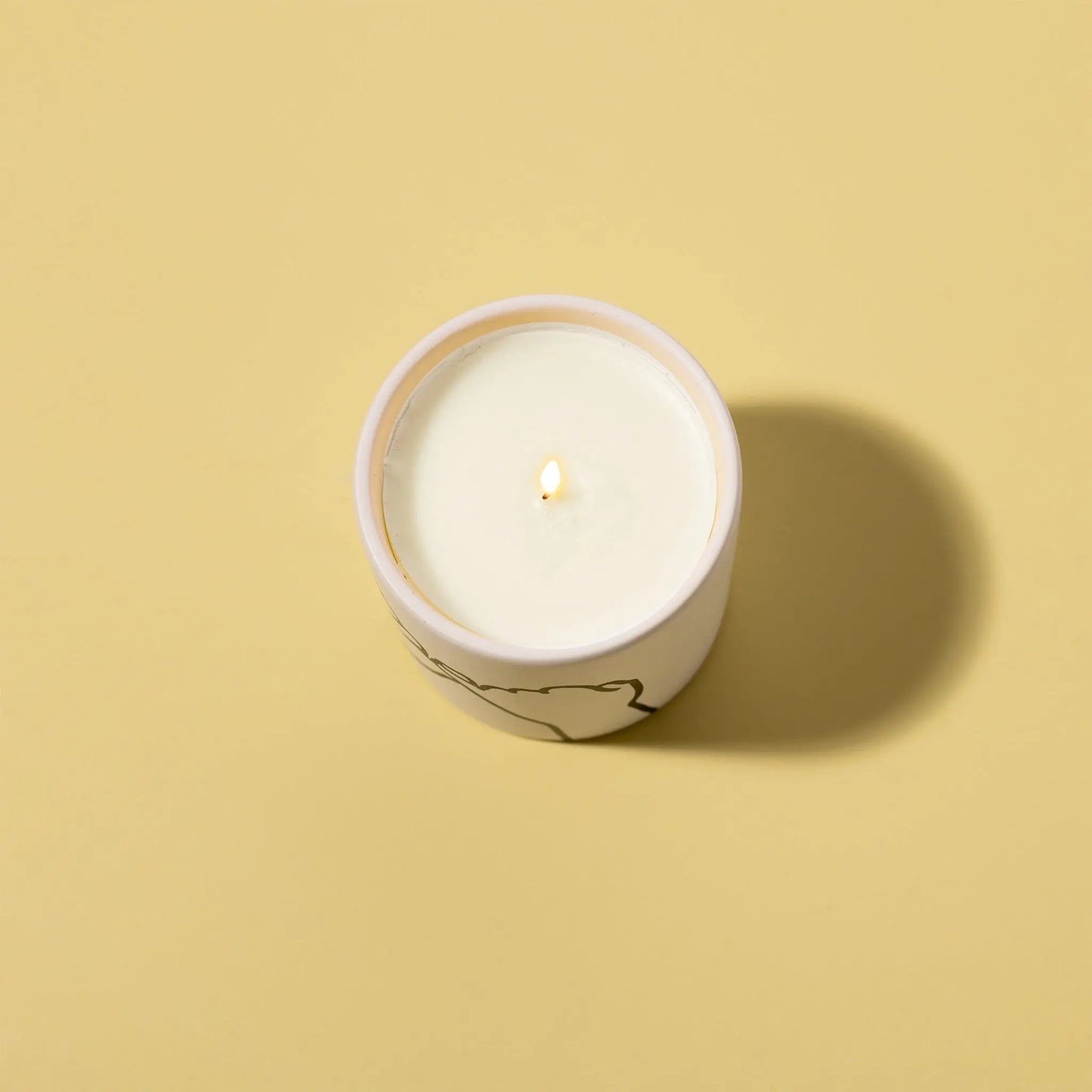 The Wild Fig + Cedar "Pinky Promise" - Impressions 5.75 oz Candle is lit in a round container on a plain beige background, casting a shadow to the right.