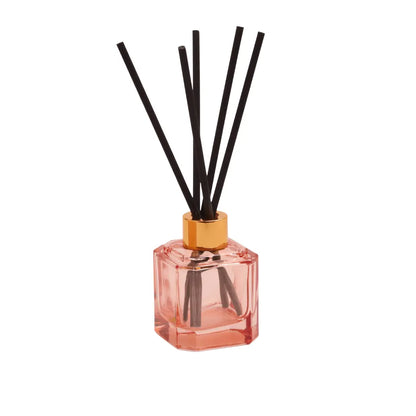 The Saffron Rose - Botanica Diffuser 2.88 oz features a pink glass design with a gold cap and black reeds, filling your space with an elegant saffron rose scent—a modern home fragrance statement against a white background.