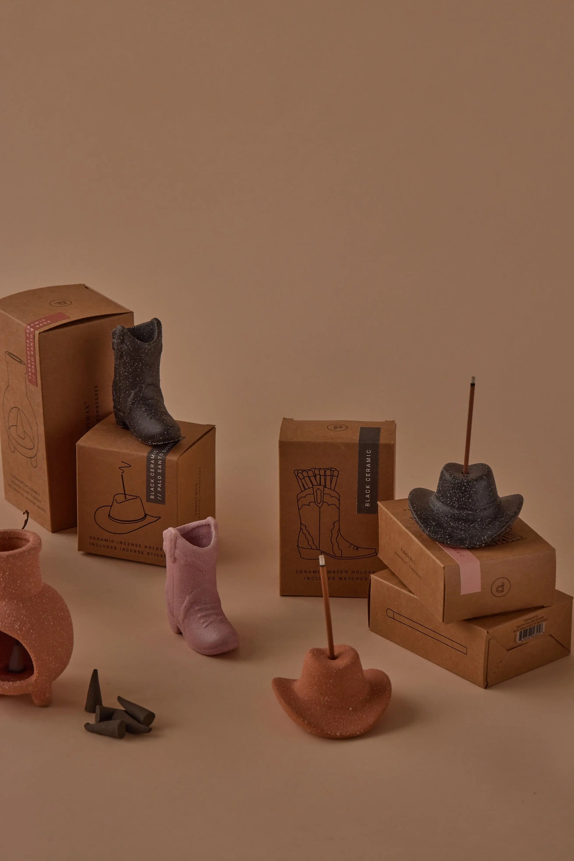 Palo Santo Suede - Incense Holders shaped like cowboy boots and hats are arranged with incense sticks on cardboard boxes, evoking a Nashville-inspired decor scene against a beige background.