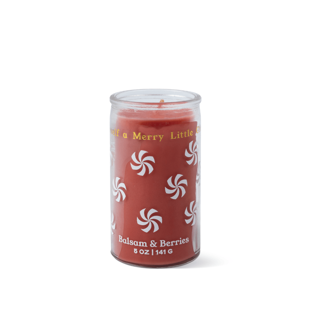 A red glass jar candle featuring white peppermint swirl designs, labeled “Balsam & Berries - 5 oz Candle” with gold text encircling the top rim. Set against a white background.