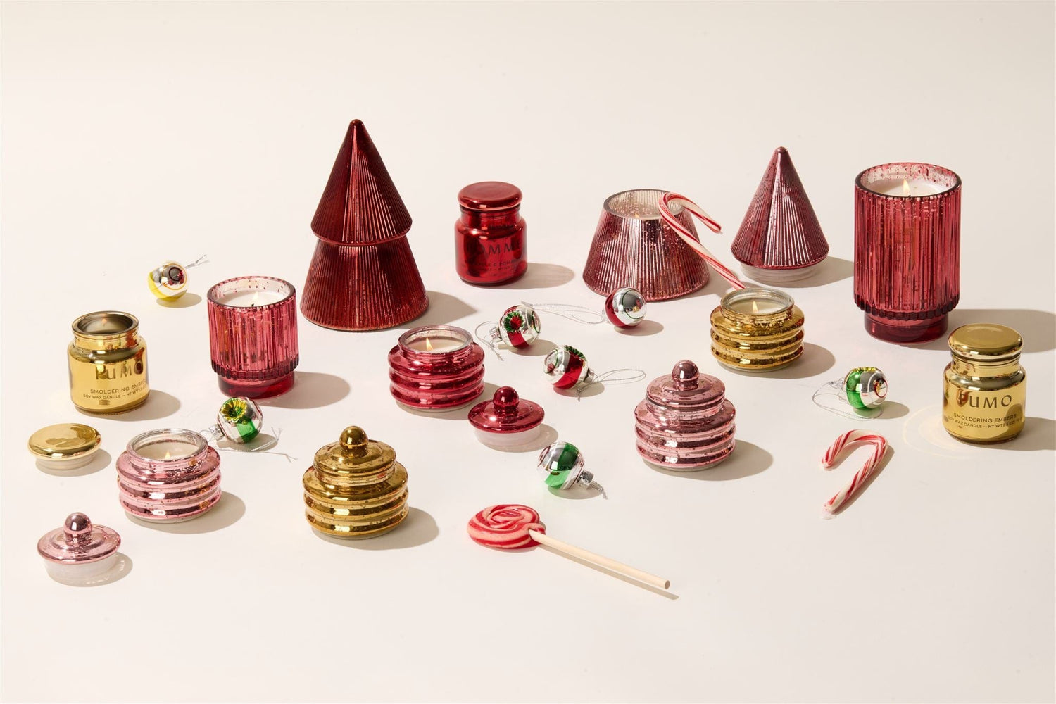 An assortment of red and gold holiday candles, jars, candy canes, small ornaments, and a lollipop arranged on a white surface.