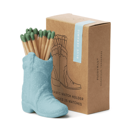 The Cowboy Boot Match Holder - Light Blue is a charming Nashville decor piece, featuring green-tipped matches and vintage-inspired style. It comes with 25 matches in a brown box labeled "Ceramic Match Holder Includes 25 Matches.