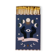 A Dopo "Moon" - 75ct Boxed Matches: Gold-tipped safety matches in a dark blue box with mystical designs—two black hands, an eye, moon phases, stars, and a pink "75 MATCHES" banner. Ideal for lighting your A Dopo candle or bringing Mediterranean vibes.