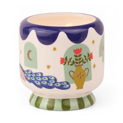 Showcase the Misted Lime - A Dopo 8 oz Candle in this colorful ceramic holder, featuring painted windows, stars, a peacock, floral vase, and green-striped base. Perfect for hand-painted candles; watch as the candle glows beautifully inside.