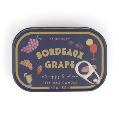 The Bordeaux Grape - Bistro 4.5 oz Tin Candle features colorful illustrations of grapes, figs, a croissant, a drink, and a wine glass on a dark background. A pull-tab lid adds charm to this Bistro-scented tin candle.