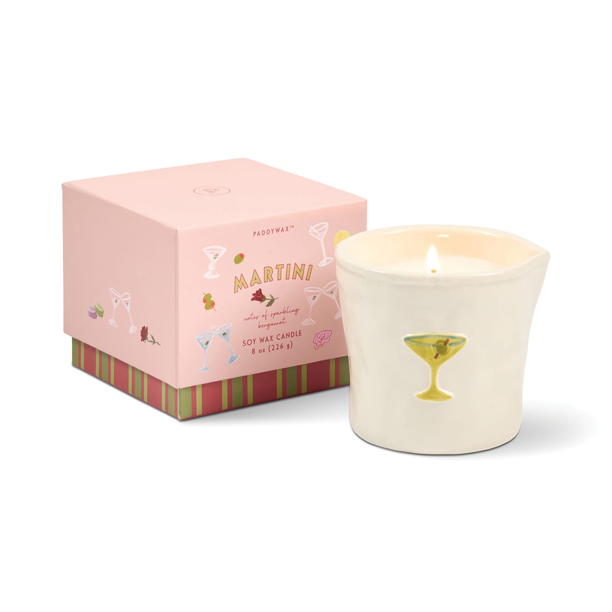 A lit Martini - Bistro 8 oz Candle, featuring a white wax in a cup adorned with a gold martini glass design, is placed next to its pink Martini-scented candle box decorated with cocktail glass illustrations.