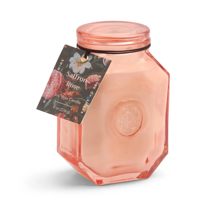 A pink hexagonal glass jar holds our Saffron Rose - Botanica 8 oz Candle, a pale pink soy wax candle with a floral tag—an elegant, luxurious addition to the Botanica Collection.