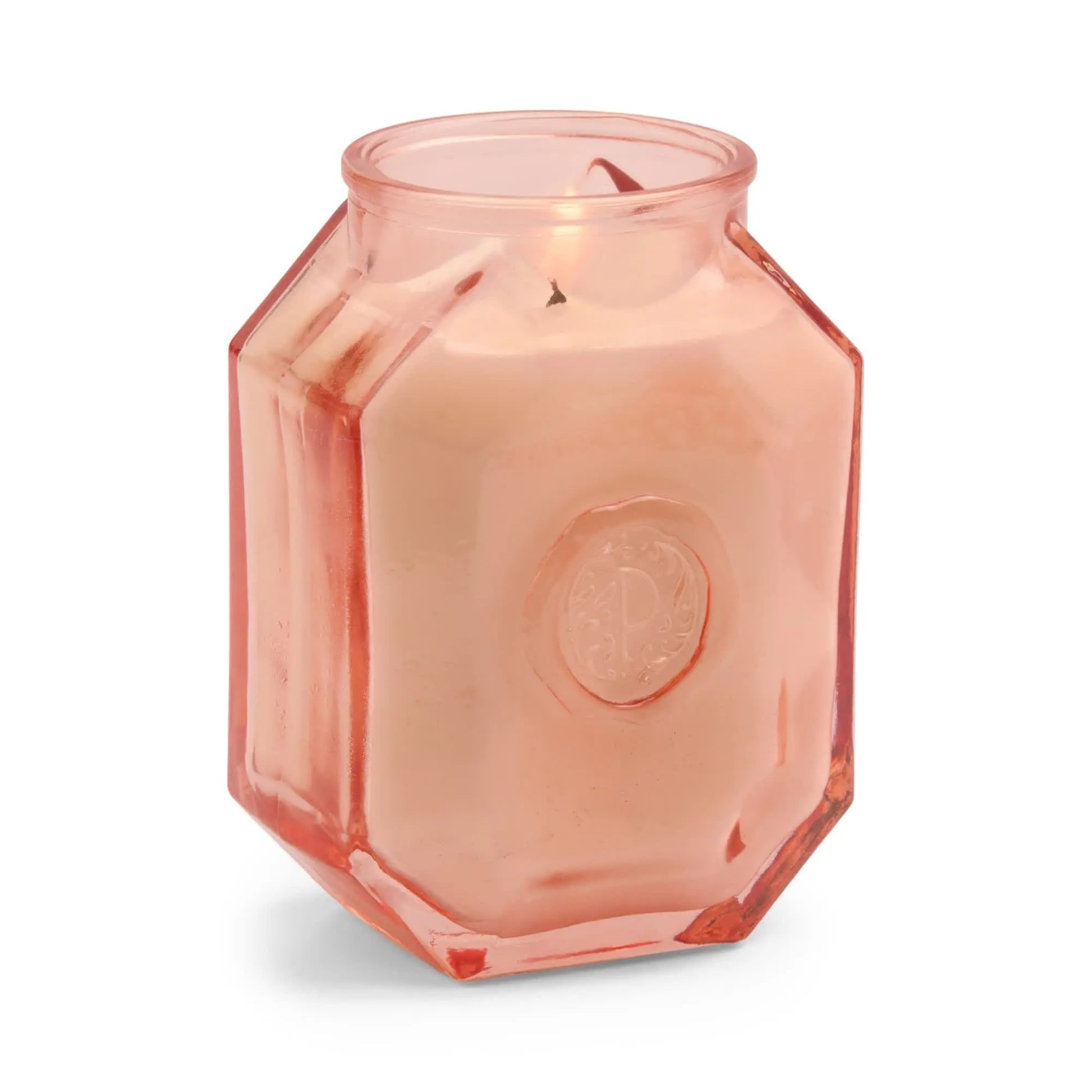The Saffron Rose - Botanica 8 oz Candle features a lit white candle in a translucent pink, faceted glass jar with a raised emblem—an elegant addition to any space.