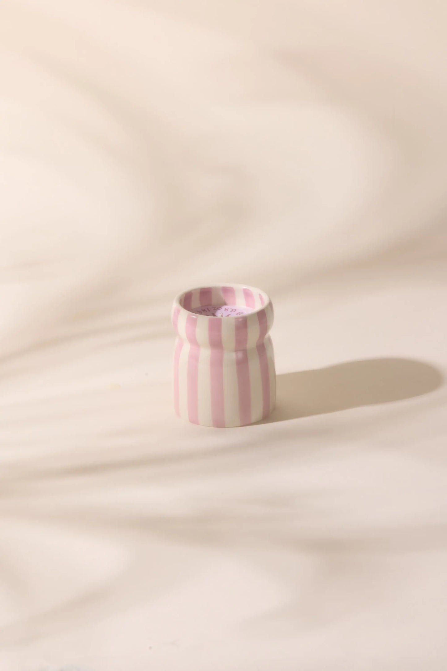The Grecian Sand - Cabana 6.5 oz Candle features a small ceramic vessel with vertical pink and white stripes, ideal for creating a relaxing coastal vibe with your favorite hand-painted candles or soothing scents.