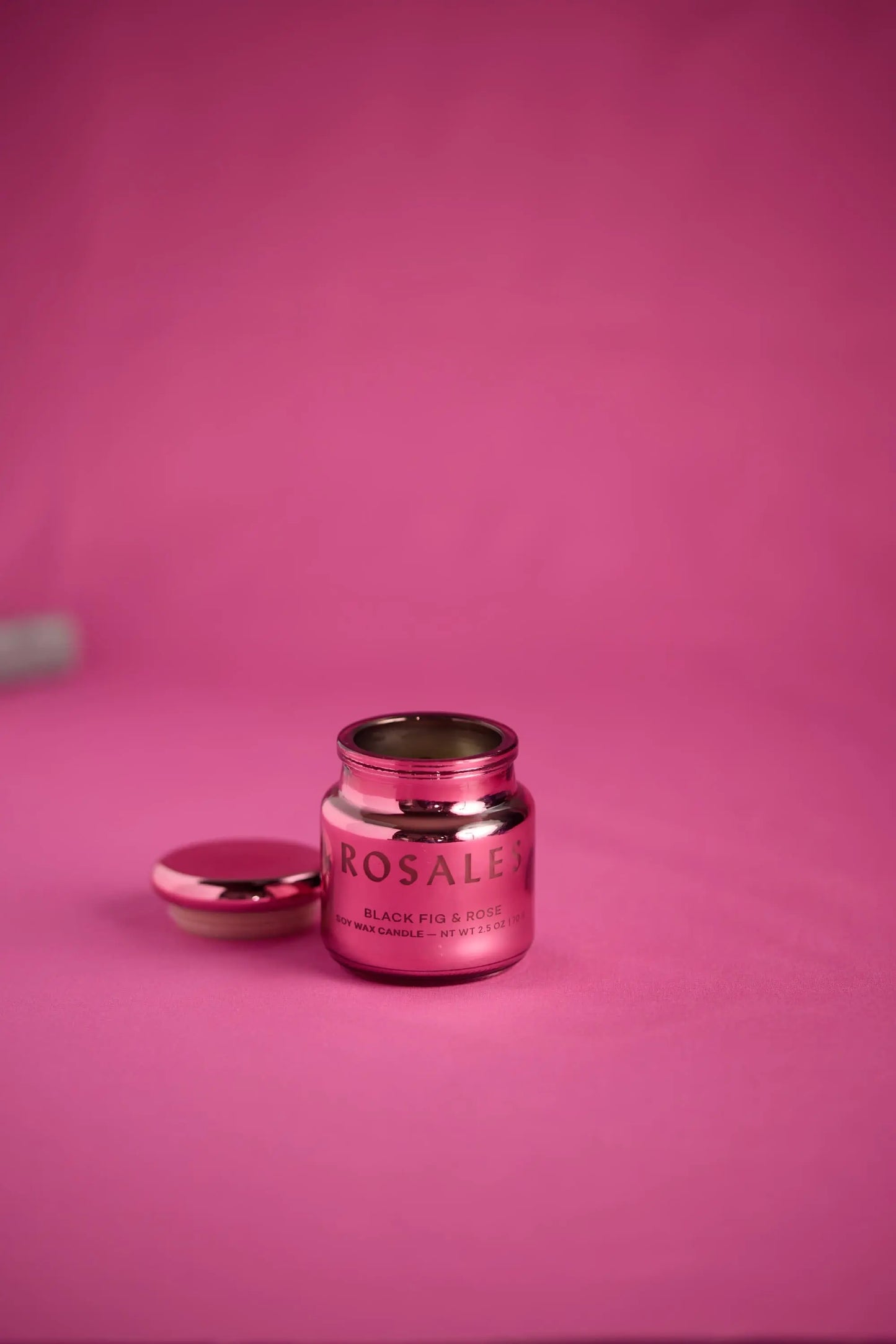 A metallic pink electroplated glass jar labeled Saffron Rose – Chroma Candle 2.5 oz sits with its lid off on a pink surface against a pink background, highlighting this vibrant candle from the Chroma collection.