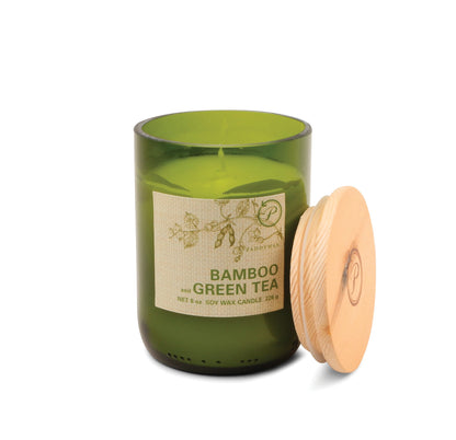 A Bamboo + Green Tea - Eco 8 oz Candle in green glass with a wooden lid sits beside it. The label highlights its soy wax blend—an ideal choice for those who value sustainable living.