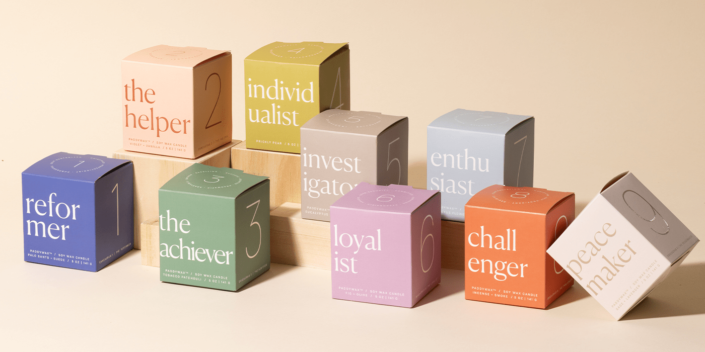 Nine pastel-colored boxes labeled with different personality types (the helper, individualist, investigator, enthusiast, reformer, achiever, loyalist, challenger, peacemaker) are arranged on a wooden display.