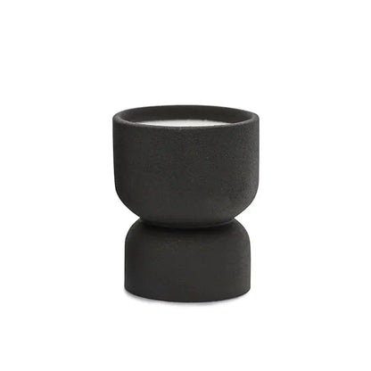 The Palo Santo Suede - Form 6 oz Candle features a small, black matte ceramic holder with a modern hourglass design. It includes a white candle and is ideal for desert-inspired decor—reuse it as a planter. Shown on a plain white background.