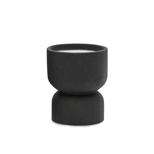 The Palo Santo Suede - Form 6 oz Candle features a small, black matte ceramic holder with a modern hourglass design. It includes a white candle and is ideal for desert-inspired decor—reuse it as a planter. Shown on a plain white background.