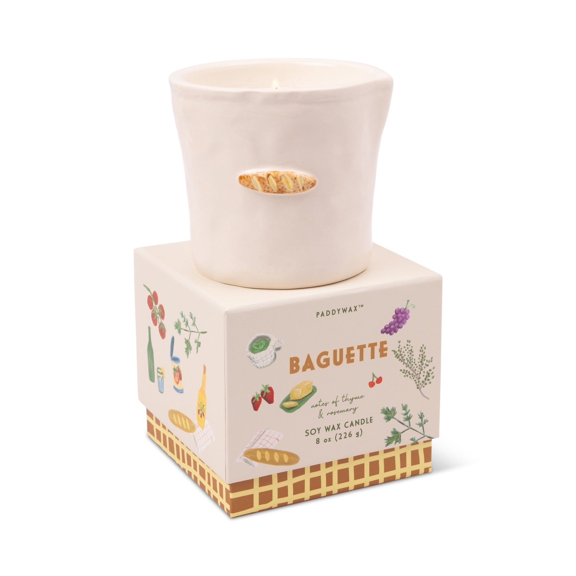 The Baguette - Bistro 8 oz Candle by Paddywax is a white ceramic holder with a small baguette design, presented on a decorative "Baguette" box featuring flowers, bread, and food art. It contains aromatic soy wax.