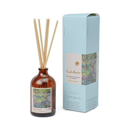 The Claude Monet Secret Garden Impressionist Diffuser (2.7 fl oz) features a brown glass reed diffuser with wooden sticks beside a blue box adorned with floral art—an ideal gift for fans of Impressionist candles and artistic home décor.