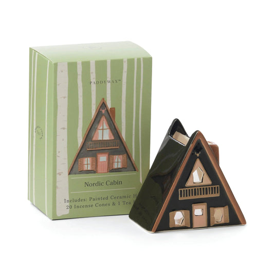 No. 01 The Nordic Cabin - Incense & Tea Light Holder is a painted ceramic A-frame cabin beside its green box, which features an illustration and Nordic Cabin text—ideal for adding Scandinavian style to your decor.