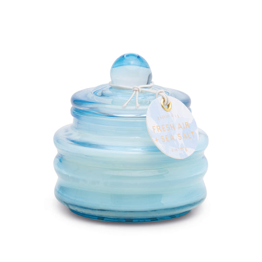 A round, light blue glass jar with horizontal ridges and a matching lid holds the Fresh Air & Sea Salt - Beam 3 oz Candle. A white tag labeled "Fresh Air & Sea Salt" is attached to the lid.