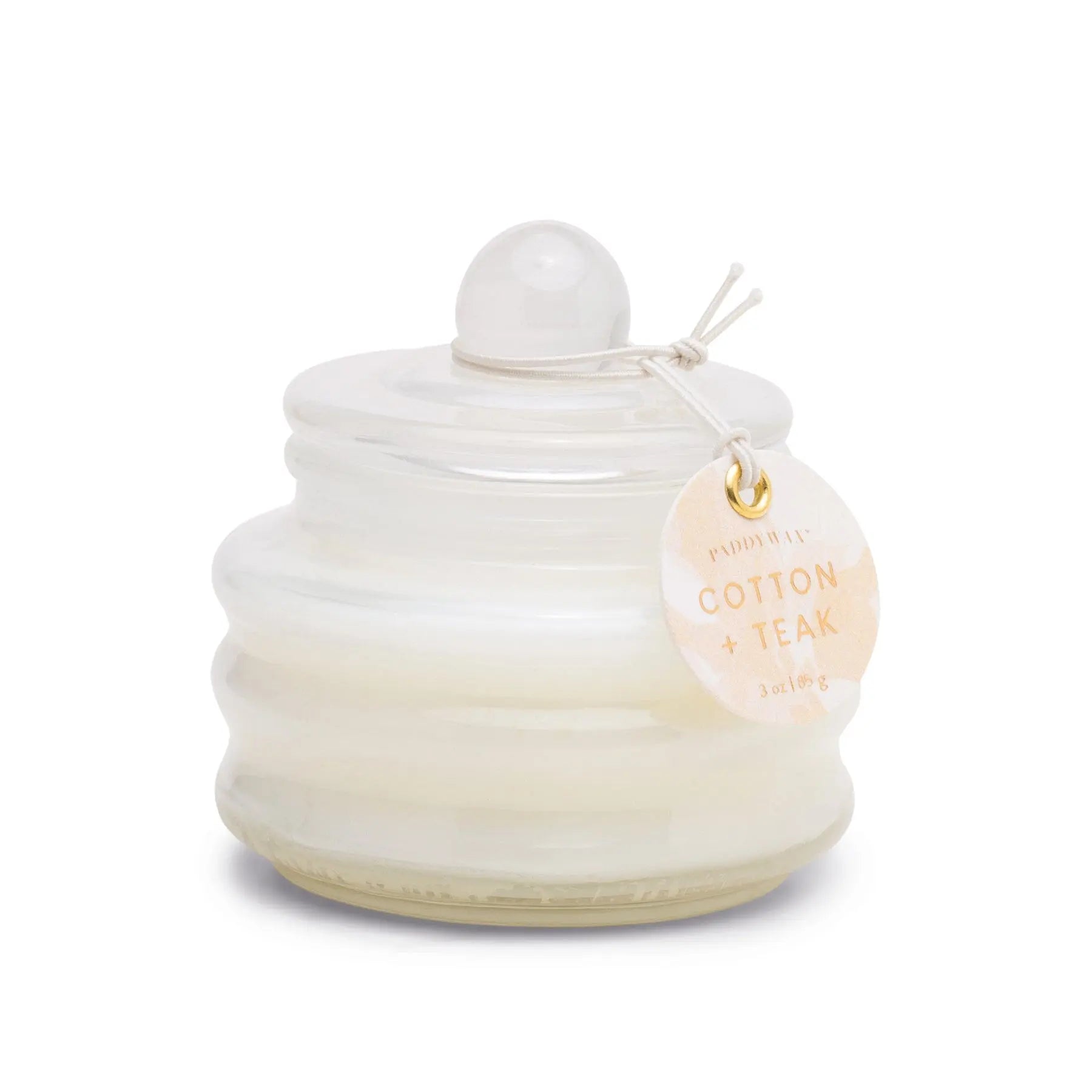 The Cotton & Teak - Beam 3 oz Candle is a small, white glass jar with a lid and tag. This luxury scented candle adds ambient light and elegance to any room.
