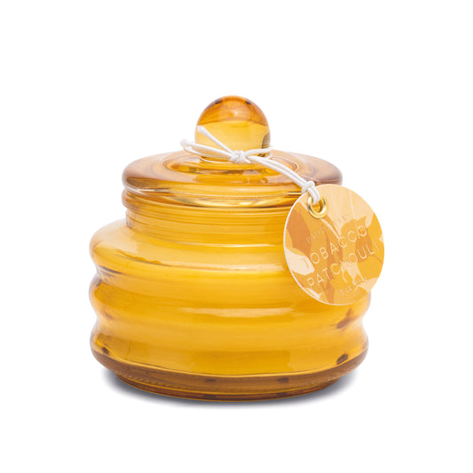 A round amber glass jar candle, the Tobacco Patchouli - Beam 3 oz Candle, features a lid and a white string attached to a circular tag labeled "Tobacco Patchouli.
