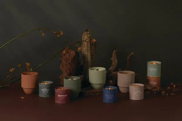A Yellowstone - Parks 6 oz Tin Candle sits on a surface with dried branches and wood pieces in the background.