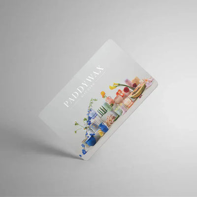 A Paddywax gift card featuring various colorful candles and decorative items arranged in a row on a light background.