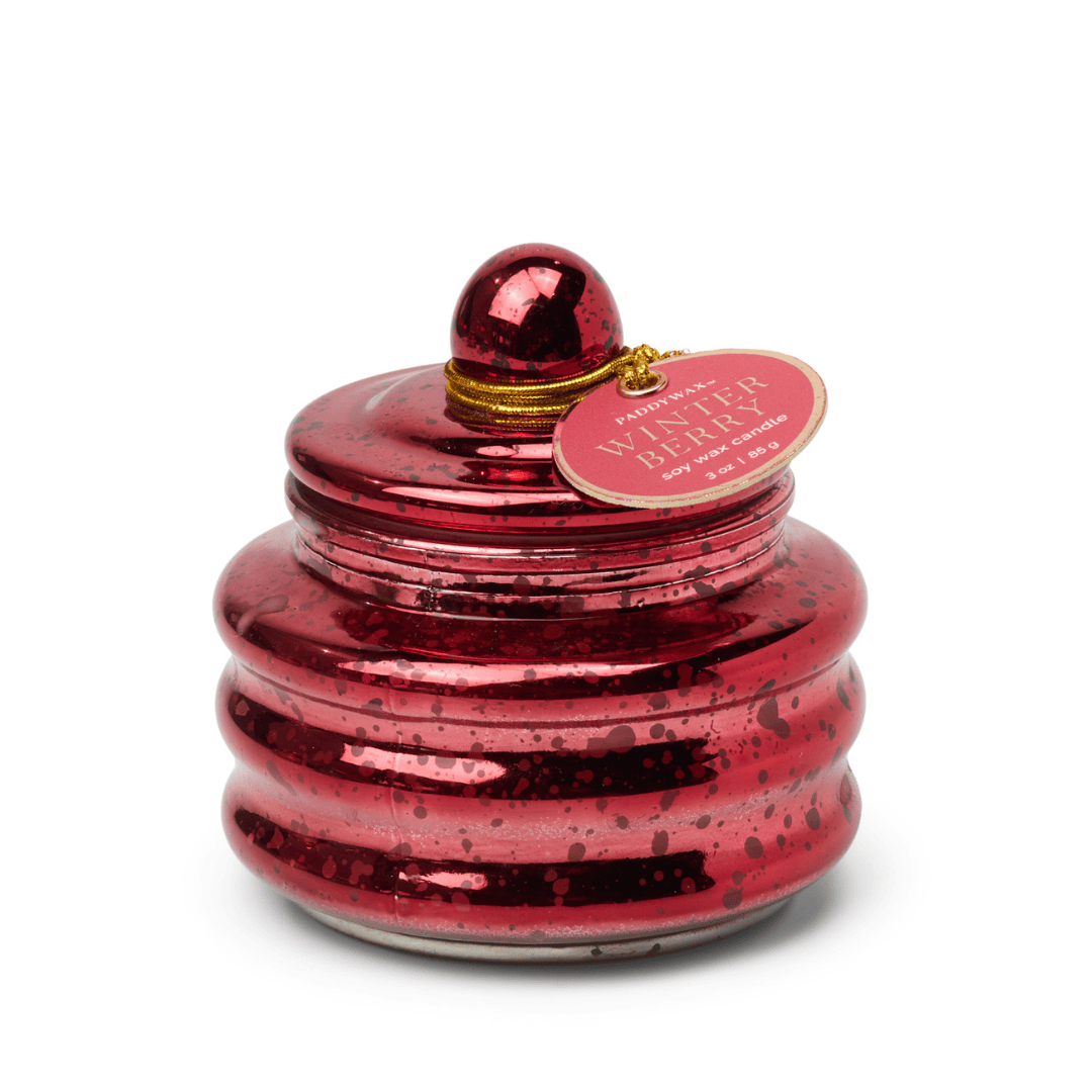 The Winter Berry - Beam 3 oz Candle features shiny red, ribbed glass with a round lid and gold string holding the label. Its speckled, reflective finish makes it ideal for holiday gifting or stocking stuffers, shown on a white background.