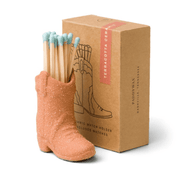 The Cowboy Boot Match Holder - Terracotta, filled with blue-tipped matches, sits before a brown box with an illustrated boot—an ideal Nashville gift or charming addition to Western-themed home decor.