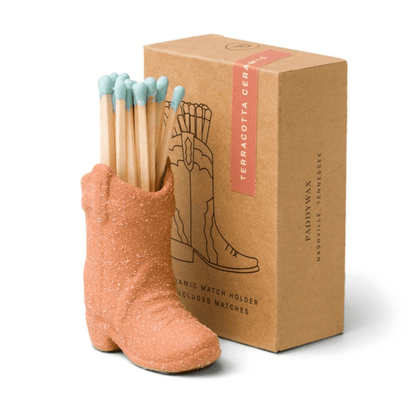 The Cowboy Boot Match Holder - Terracotta, filled with blue-tipped matches, sits before a brown box with an illustrated boot—an ideal Nashville gift or charming addition to Western-themed home decor.