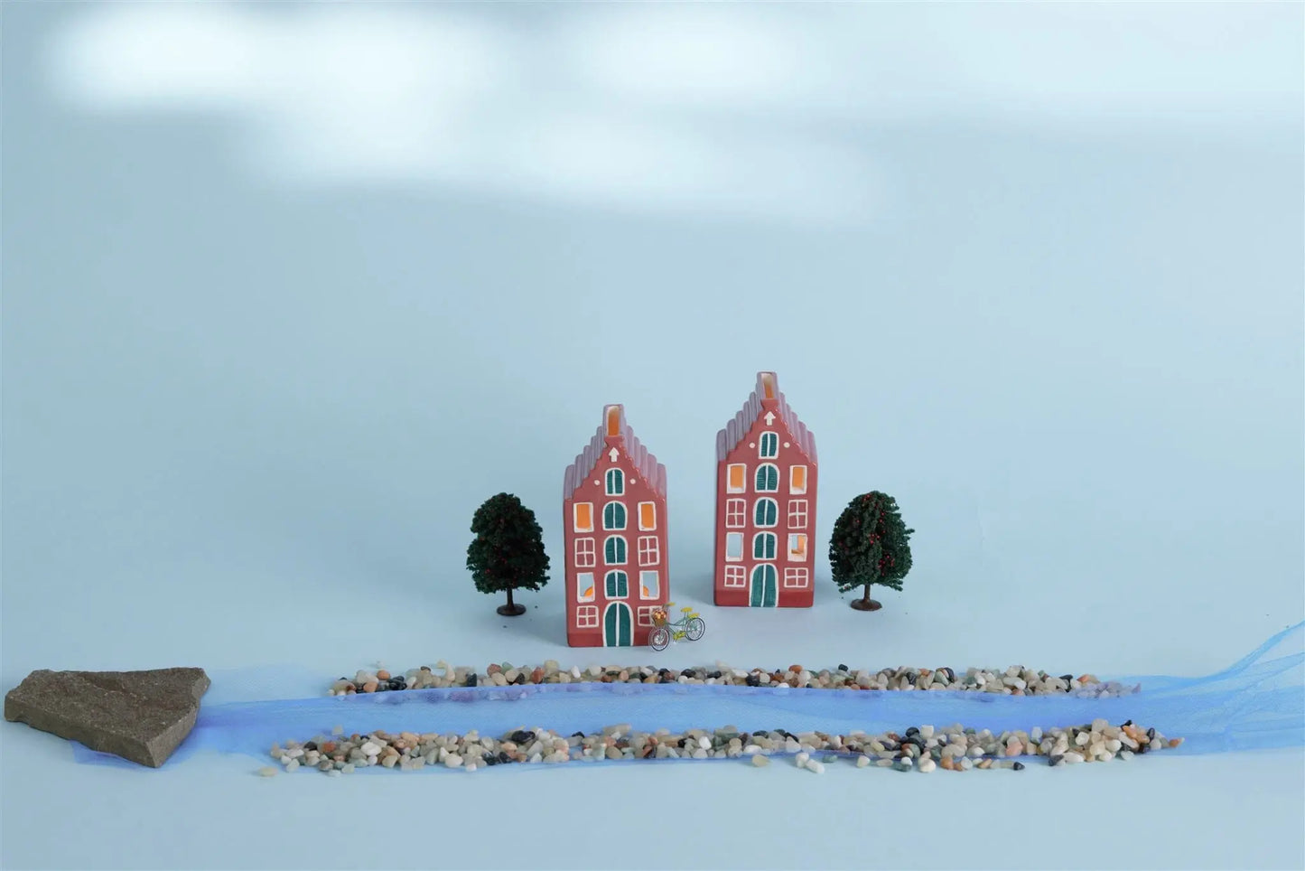 The No. 02 The Amsterdam House - Incense & Tea Light Holder is displayed with trees, pebbles, a blue fabric strip, and a rock on a light surface, capturing the charm of Amsterdam canal house decor.