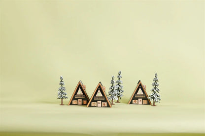 No. 01 The Nordic Cabin - Incense & Tea Light Holder is shown among pine trees and a snowy A-frame cabin village scene on a light yellow background, inspired by Scandinavian décor.