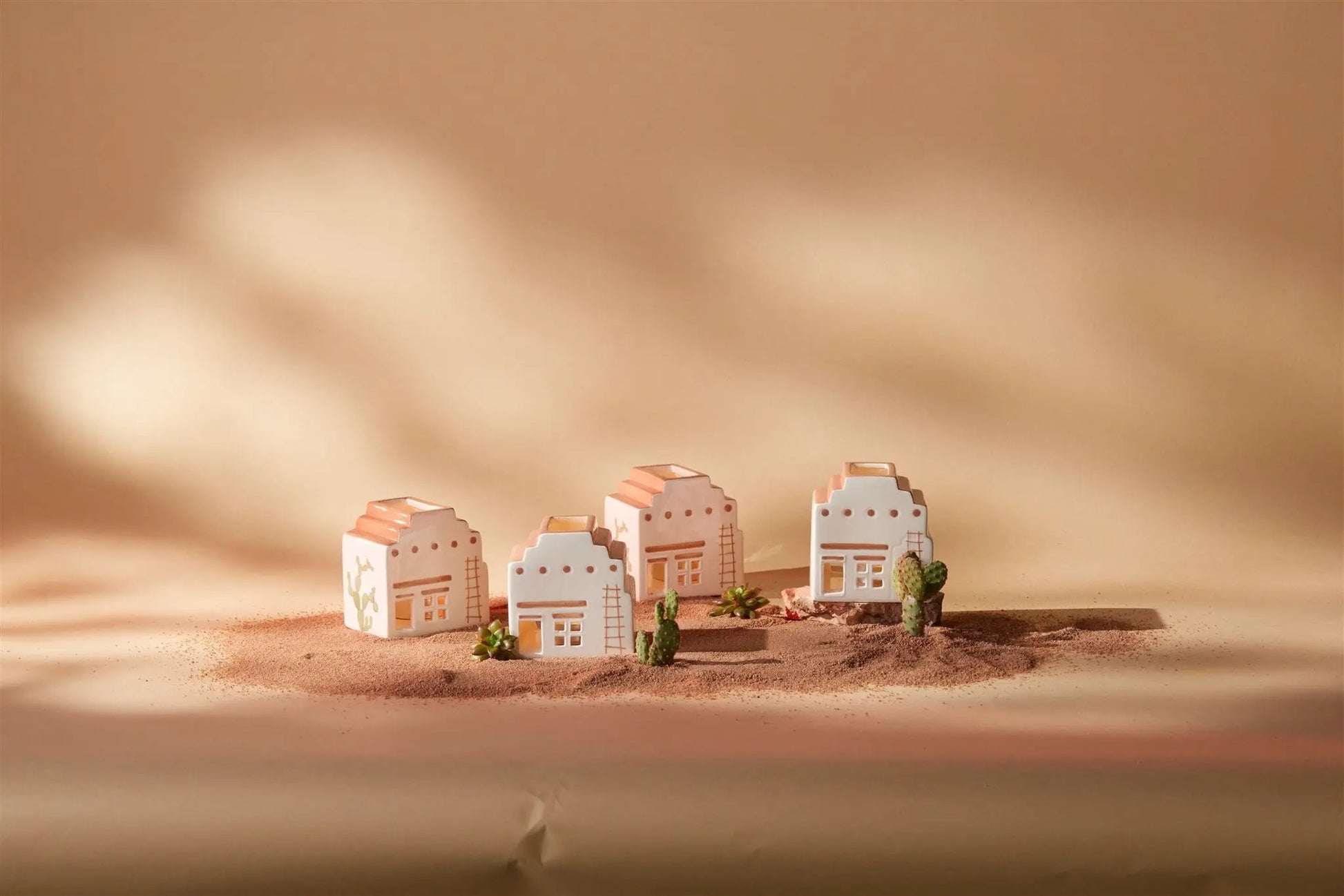 Four No. 03 The Santa Fe Adobe Incense & Tea Light Holders with pastel accents sit on sand among small cacti and plants, set against a warm beige background with soft shadows.