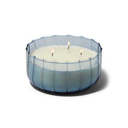The Peppered Indigo - Ripple 12 oz Candle features three wicks in a round, translucent blue ribbed glass container, shown against a white background.