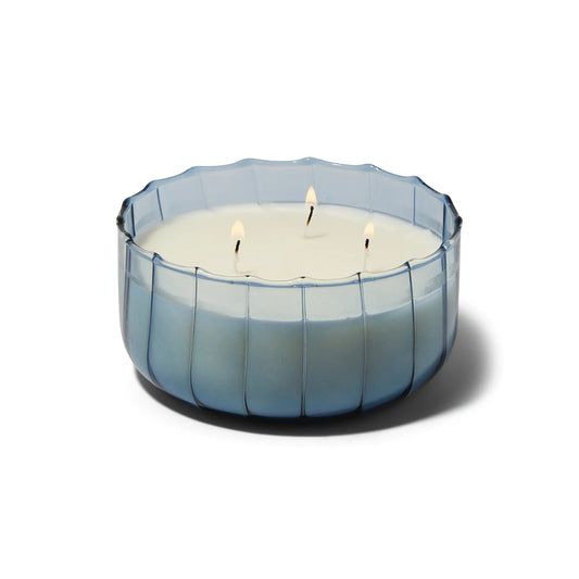 The Peppered Indigo - Ripple 12 oz Candle features three wicks in a round, translucent blue ribbed glass container, shown against a white background.