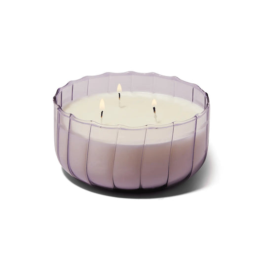The Salted Iris - 12 oz Candle features three wicks ablaze in a round, translucent ribbed glass container, viewed at an angle against a white background.