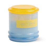 A light blue reusable glass jar candle with a rounded, ribbed base and bright yellow lid. The front label reads “Zesty Lemon - Stack 7 oz Candle,” emphasizing its citrus scent and refreshing aroma.