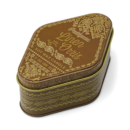 A decorative, paisley-patterned brown and gold travel-sized station tin candle labeled Linen & Orris - Station Tin 3.5oz, featuring a uniquely rounded triangular shape and a slightly askew lid—perfect for bringing warm, woody scents inspired by Northern California anywhere you go.