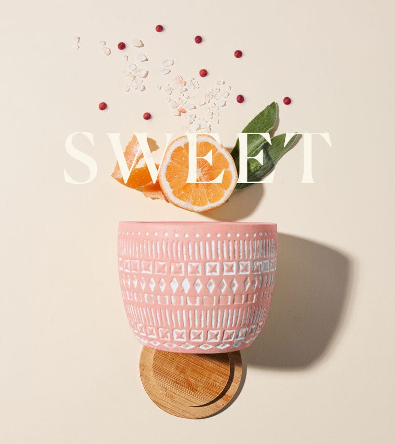 A pink patterned cup sits on a wooden coaster with orange slices, green leaves, grains, and red berries scattered nearby. The word SWEET is overlaid in large white text.