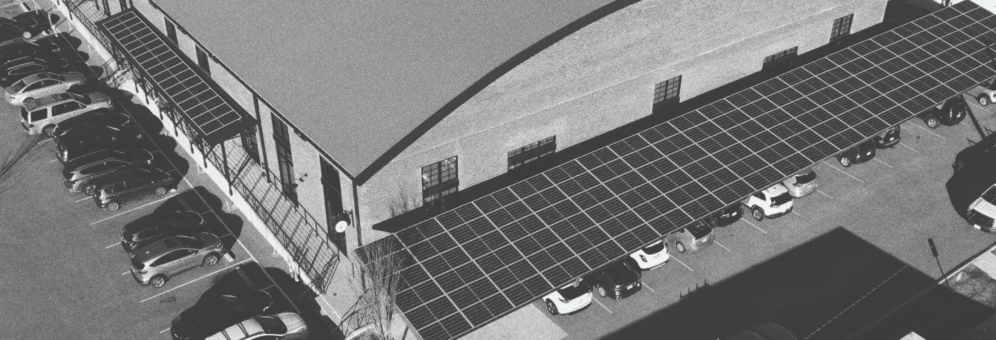 Aerial view of a parking lot with cars parked under solar panel canopies next to a large building.