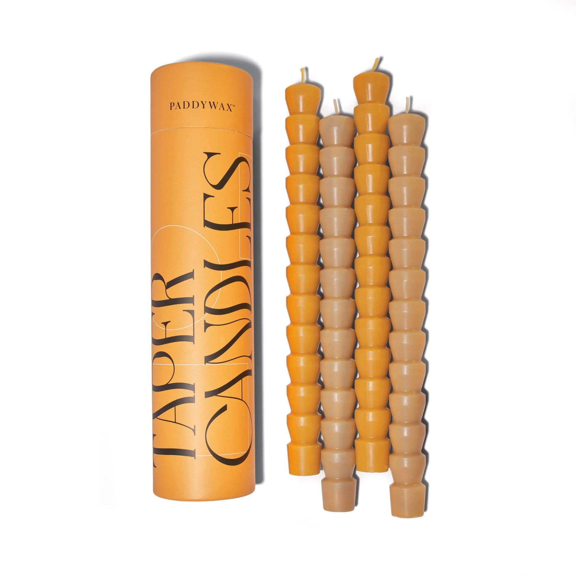 A yellow cylindrical container labeled Burnt Orange & Peach Tube Tapers - Set of 4 sits beside four stacks of small, sleek orange tapers—ideal for sophisticated dining settings.