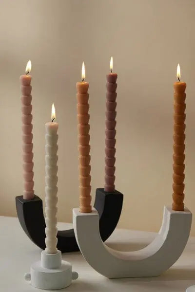 Four spiral taper candles in pink, beige, and brown stand in modern U Taper Holders—two black, two white (U Taper Holder - White)—against a neutral background.