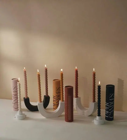 A row of lit, sleek Burnt Orange & Peach Tube Tapers (set of 4) in modern holders, with their cylindrical packaging behind—an elegant choice for sophisticated dining settings.