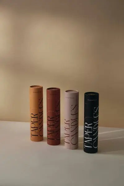 The Red & Terracotta Tube Tapers - Set of 4 stand upright on a light surface, featuring elegant lettering and contemporary colors—perfect for stylish table settings.