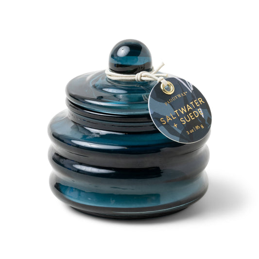 A blue, round, ribbed ceramic jar contains the Saltwater & Suede - Beam 3 oz Candle. It features a glossy finish, a lid with a twine accent around the knob, and a tag that reads SALT WATER + SUEDE.