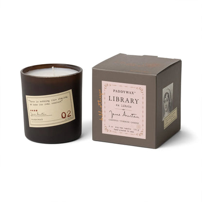 The Jane Austen - Library Candle 6 oz in a dark glass jar sits beside its brown Paddywax Library Collection box, featuring a portrait and quote—an ideal literary gift for fans of candlelight and classic novels.