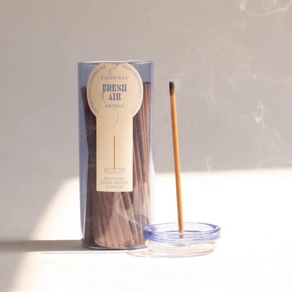 Blue glass cylinder with white label holding 100 incense sticks for flameless fragrance; pictured next to burning incense stick